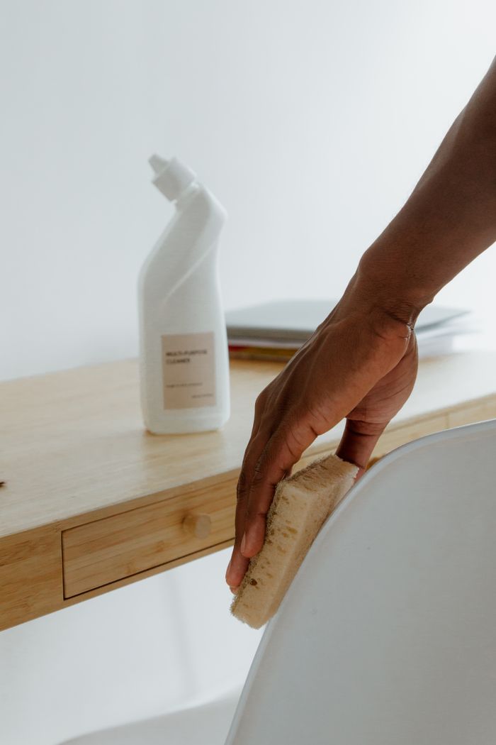 mission-img Minimalist room with a person cleaning a chair using a sponge and cleaning product.